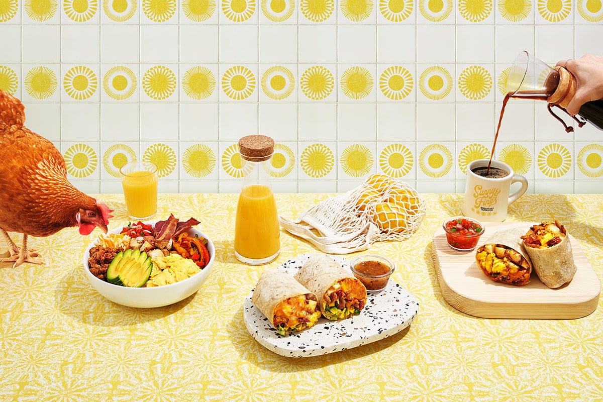 Breakfast Spread with a Rooster on the Left Looking Over a Bowl, Orange Juice, and Breakfast Burritos As A Hand Pours Coffee Into a Cup