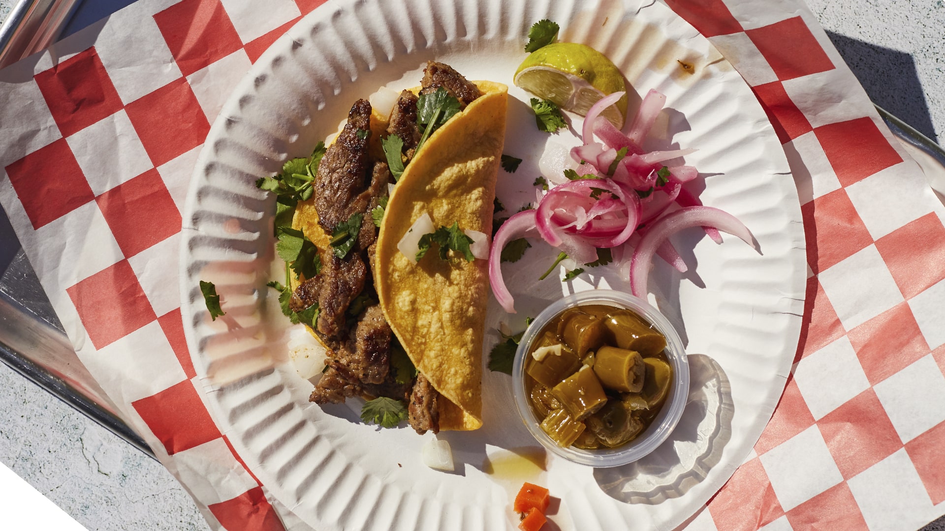 Steak taco with jalapenos and onions on a paper plate and checkered parchment paper